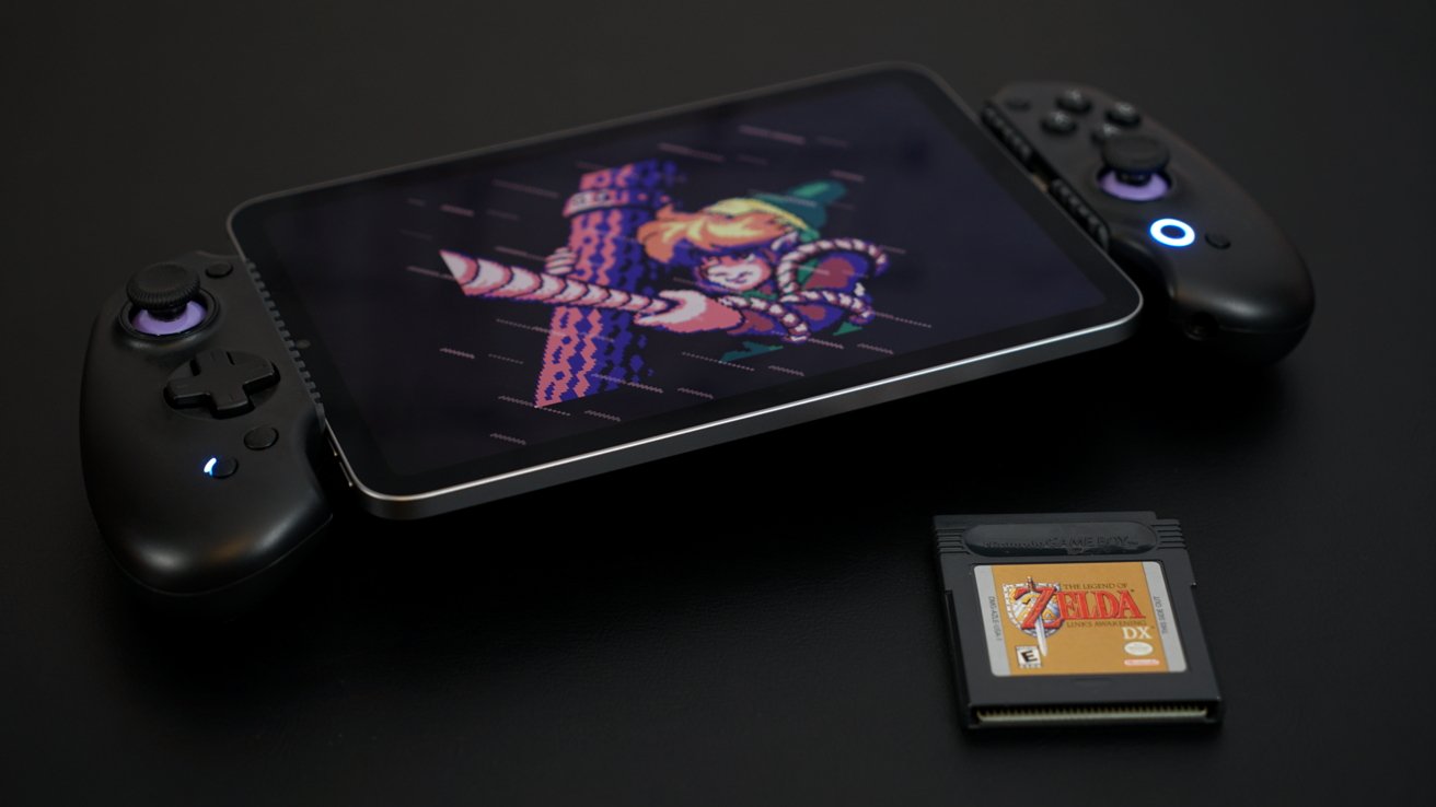 Tablet with retro video game screenshot, black gaming controllers attached, and a game cartridge labeled 'Zelda DX' on a dark surface.
