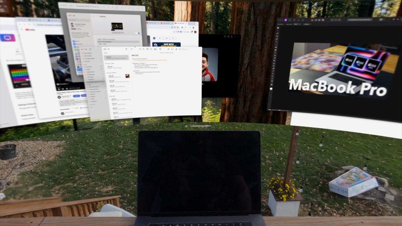 Laptop on a wooden table outside, surrounded by floating virtual windows and a garden with trees in the background.