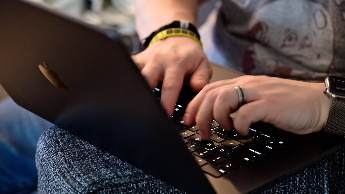 Hands typing on a laptop keyboard, wearing a ring and smartwatch, with blurred background.