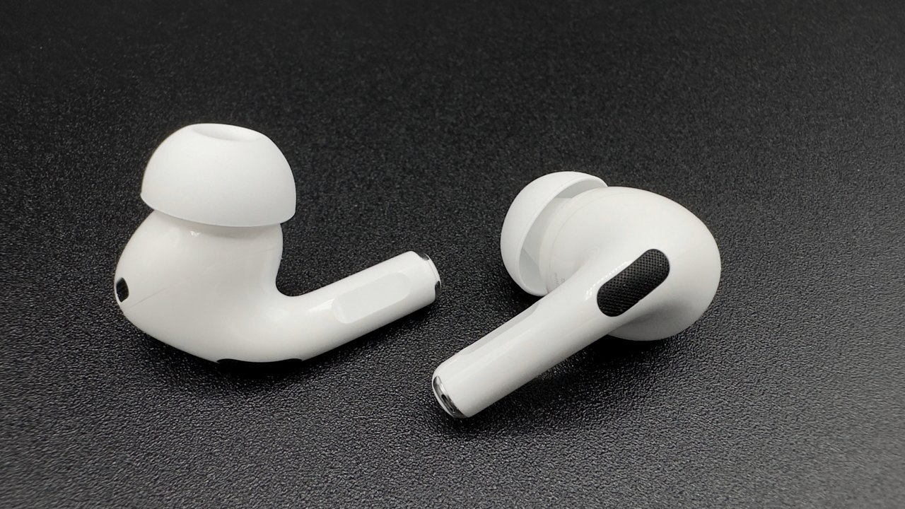 Two white wireless earbuds with silicone tips on a black surface.