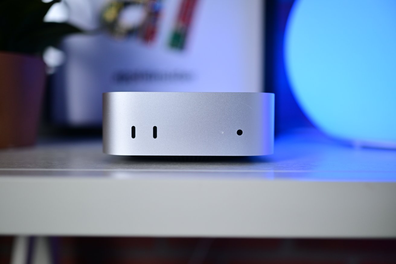 Silver, compact computer on a white shelf with blurred background featuring out-of-focus colors and shapes.