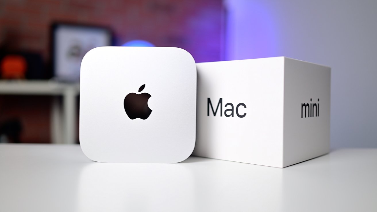 Square silver computer with Apple logo next to a white box labeled 'Mac mini' on a white surface.