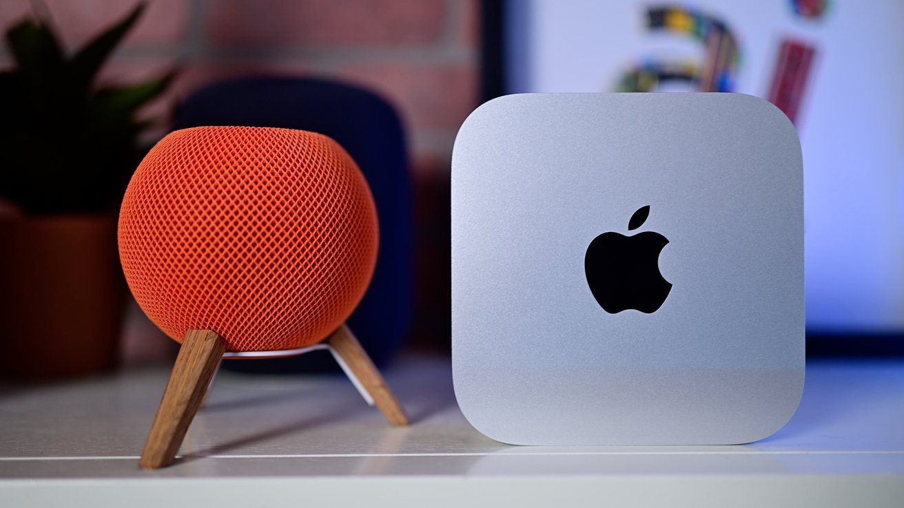 Orange spherical speaker on wooden stand beside a silver square device with an apple logo, blurred background.