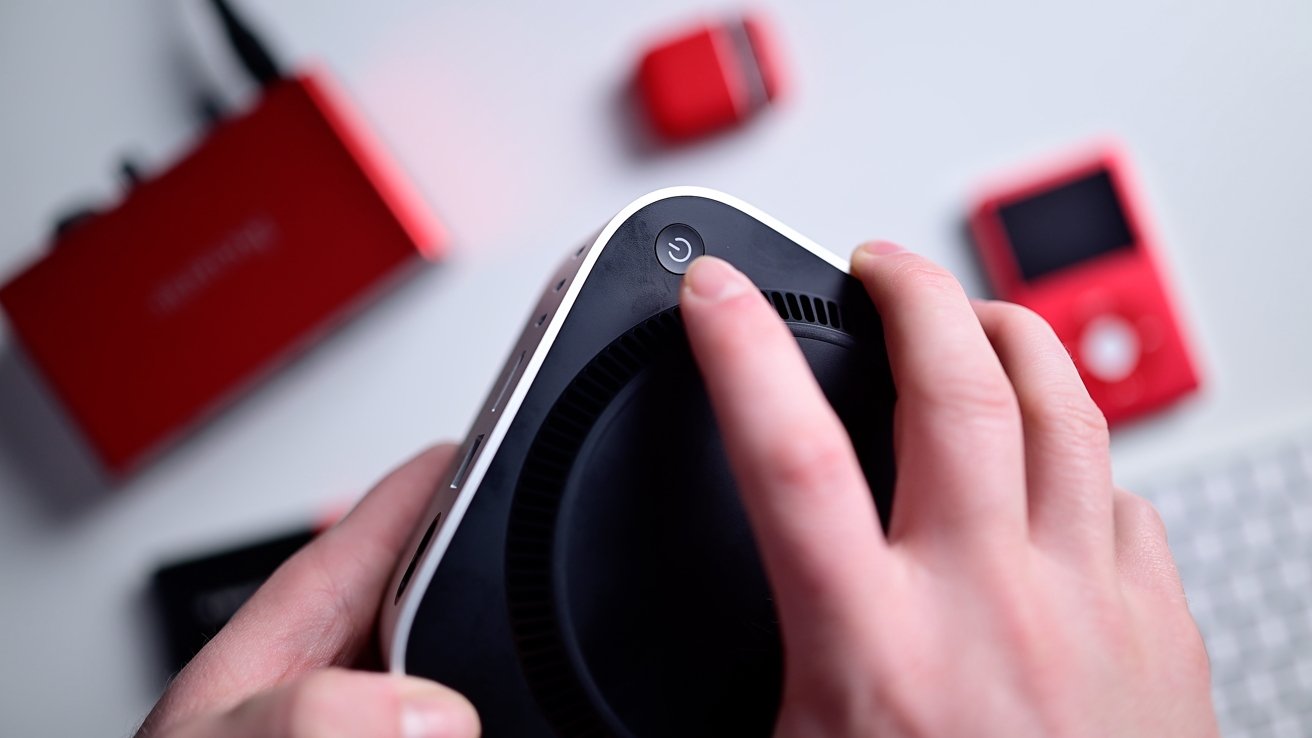 Close-up of hands pressing the power button on a black and white electronic device, with red objects blurred in the background.