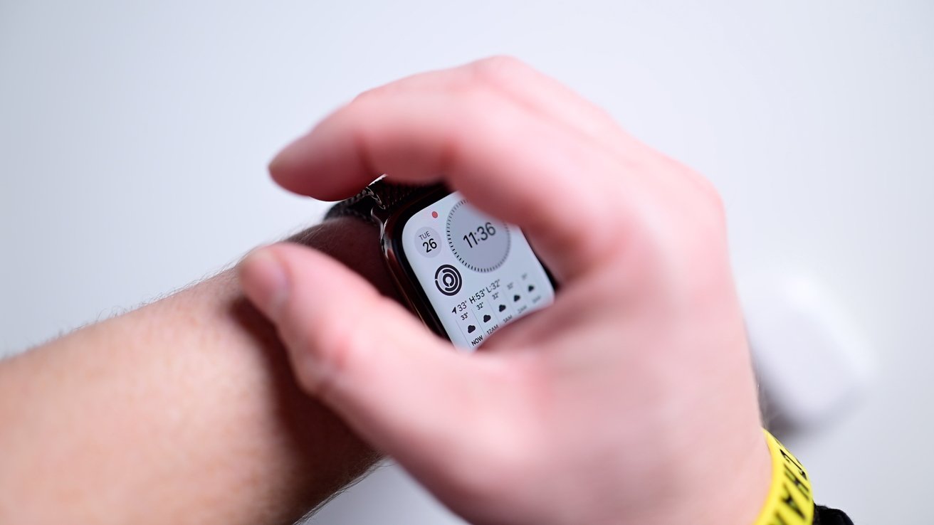 A person adjusts a smartwatch displaying the time, date, and weather information on their wrist, with a yellow wristband visible.