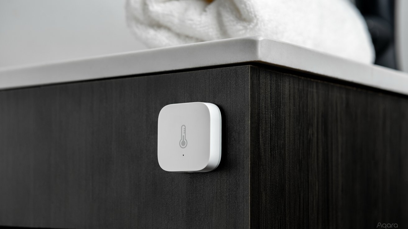 A white, square temperature sensor mounted on the side of a dark wood cabinet, with towels on top.